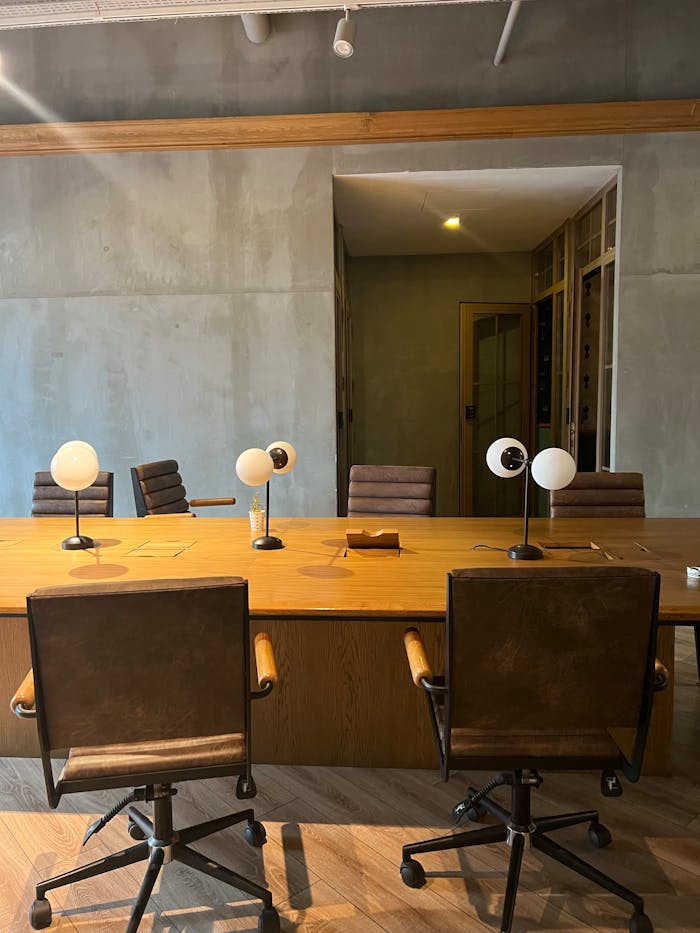 Servicios Contemporary office space in İstanbul featuring a wooden table, chairs, and desk lamps against a concrete backdrop.